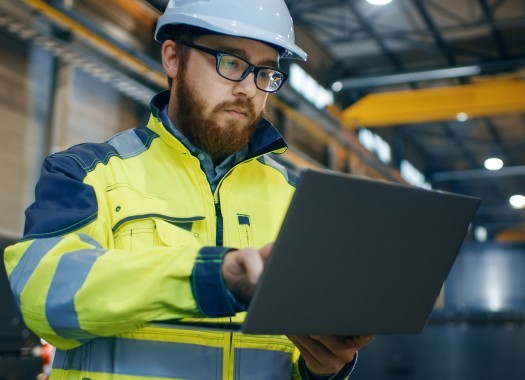 Industrial Engineer in Hard Hat Wearing Safety Jacket Uses Touchscreen Laptop  